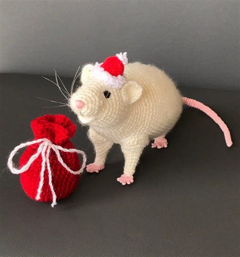 a crocheted rat next to a red bag on a black surface with grey background