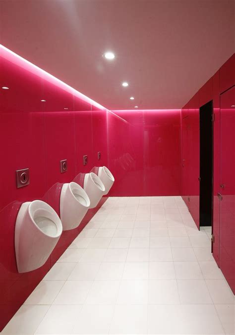 a row of urinals in a bathroom with red walls and white flooring