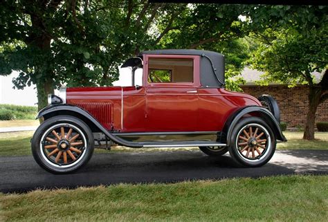 an old red car is parked on the side of the road in front of some trees