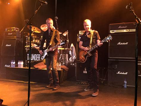 two men playing guitars on stage with microphones in the foreground and other instruments behind ...