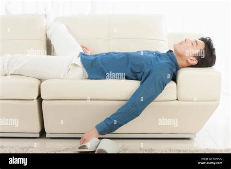 Side view of young man lying down on sofa closing eyes Stock Photo - Alamy