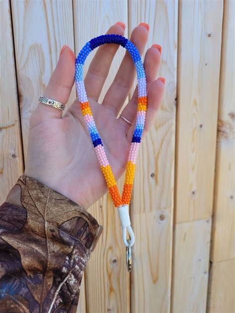 a hand holding a multicolored beaded lanyard in front of a wooden fence