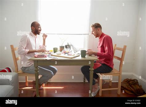 Side view of men sitting at dining table having breakfast laughing Stock Photo - Alamy