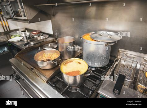 Food cooking in pots and pans on the top of a gas stove in a restaurant kitchen in Valencia ...