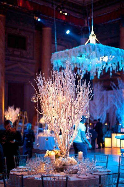 a table is set up for an event with white flowers, candles and chandelier hanging from the ceiling