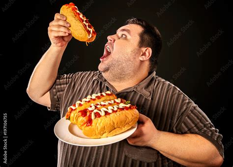 Fat man eating fast food hot dog on plate. Breakfast for overweight person. Junk meal leads to ...