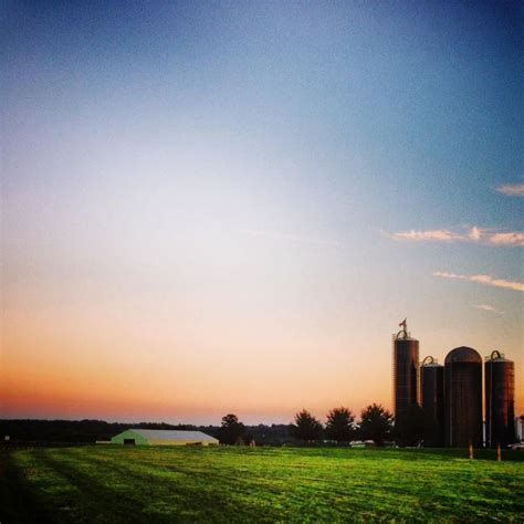 the sun is setting over a farm with silos and buildings in the back ground