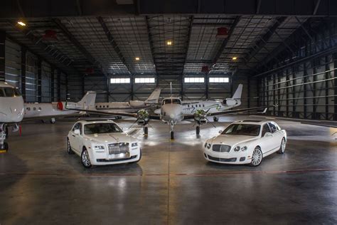 three luxury cars parked in an airplane hanger with two private jets on the far side