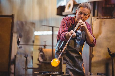 Premium Photo | Glassblower shaping a glass on the blowpipe