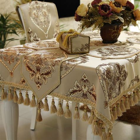 a dining room table covered with a tasseled tablecloth and some flowers in a vase