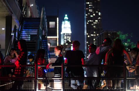 many people are standing outside at night in front of the cityscape and skyscrapers