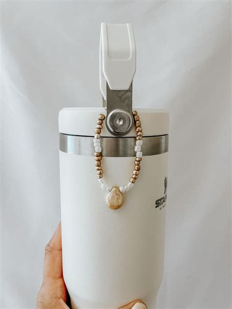 a person holding a white cup with beads and a camera attached to the top, in front of a white ...