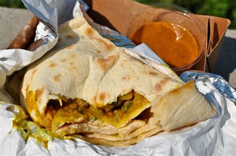 a burrito sitting on top of aluminum foil next to a bowl of sauce