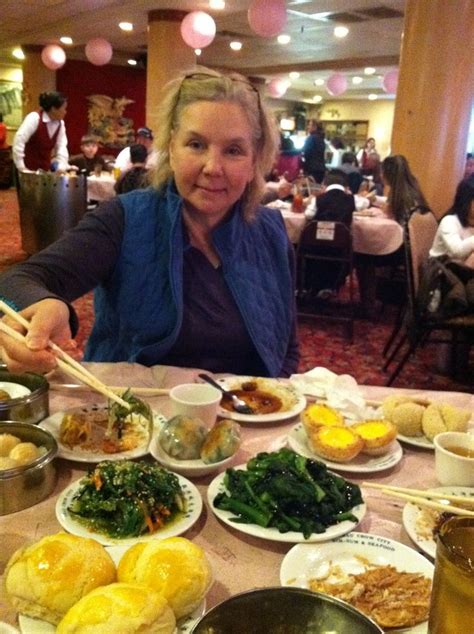 a woman sitting at a table full of food with chopsticks in her hand