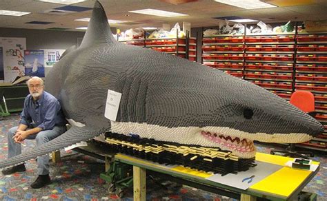 a man sitting on a bench next to a shark made out of legos in a store