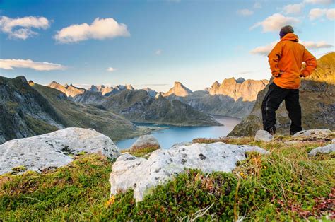 a man standing on top of a lush green hillside next to a lake in the ...