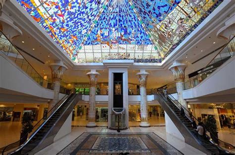 the inside of a shopping mall with colorful stained glass windows on the ceiling and escalators