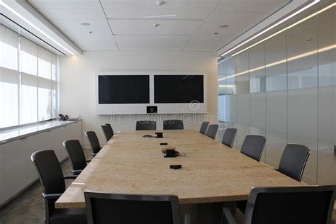 an empty conference room with chairs and a large table in front of two monitors on the wall