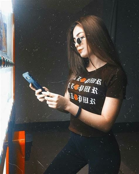 a woman wearing sunglasses looking at her cell phone while standing in front of a wall