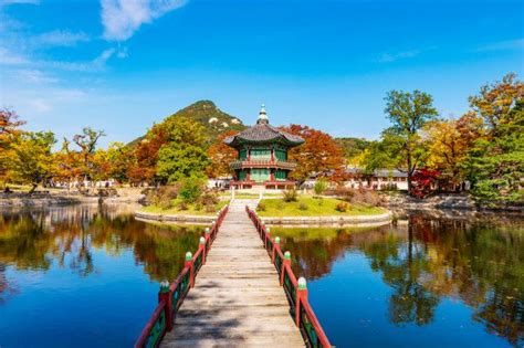 a wooden bridge over a lake leading to a pavilion with a pagoda in the background