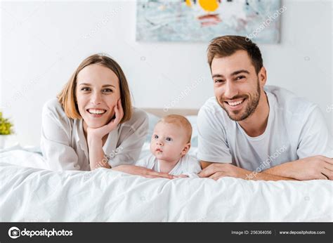 Smiling Young Parents Baby Lying Bed Looking Camera Stock Photo by ©HayDmitriy 256364056