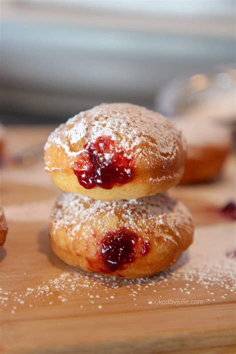 jelly donuts with powdered sugar stacked on top of a wooden board ...