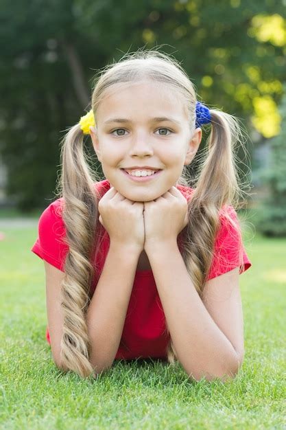 Premium Photo | Little girl cute ponytails hairstyle relaxing on green grass, summer camp concept.