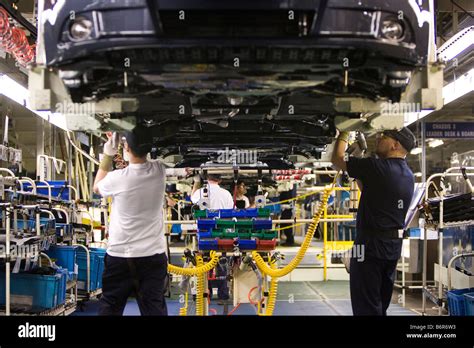 Workers at Toyota Final Assembly production line fit parts to the underside of a Toyota Avensis ...