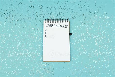 Small notebook on blue confetti background with written 2021 goals for new year. Resolutions ...