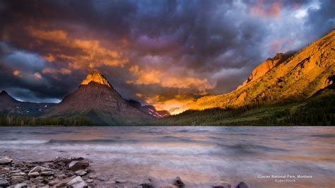 the mountains are covered in clouds and water as the sun is setting over some rocks