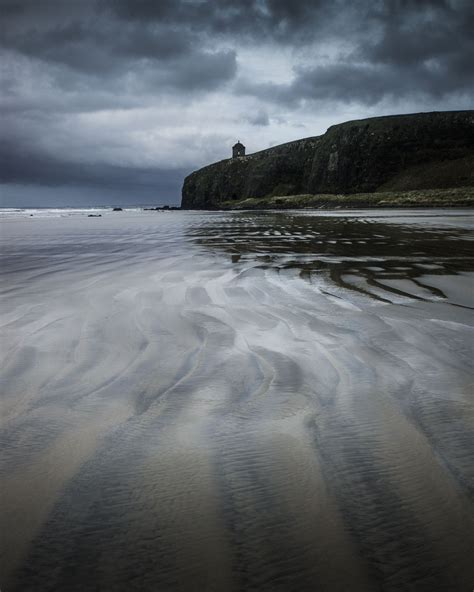 the beach is covered in sand and water under a dark sky with clouds above it