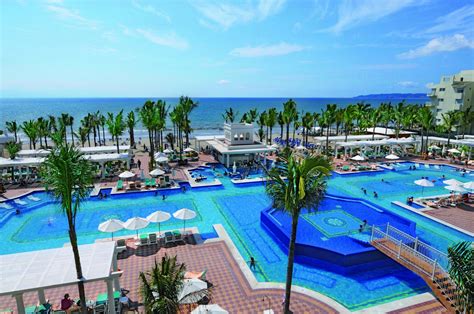 an outdoor swimming pool with palm trees and umbrellas next to the ...