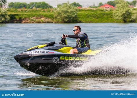 Happy BRP Sea-Doo Jet Ski Driver Drives Watercraft Splashing Outdoor at Sunset by River Bank at ...