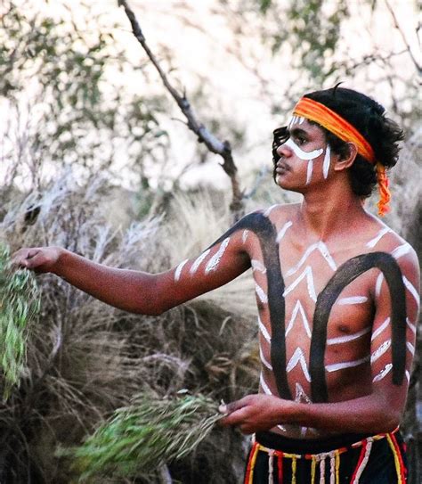 a man with white paint on his face and body standing in front of some trees