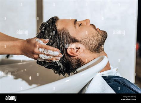 close-up partial view of hairstylist washing hair to handsome young man ...