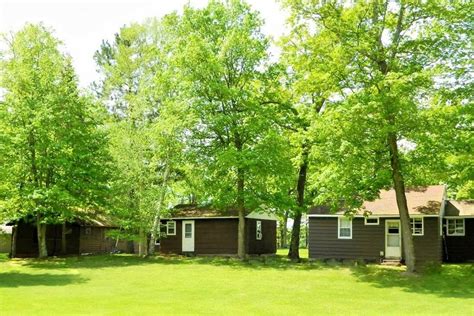 two brown cabins in the woods with trees around them and grass on the ground below