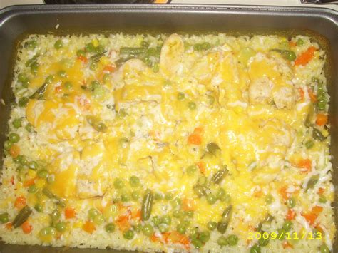 a casserole dish with chicken, rice and vegetables in it on a stove