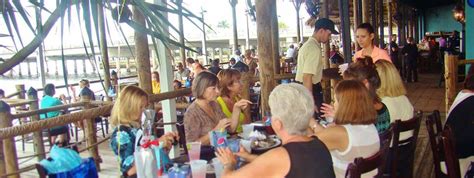 a group of people sitting at tables in front of the ocean with drinks ...