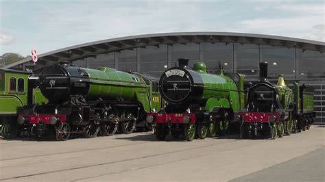 two green trains are parked next to each other in front of a large ...