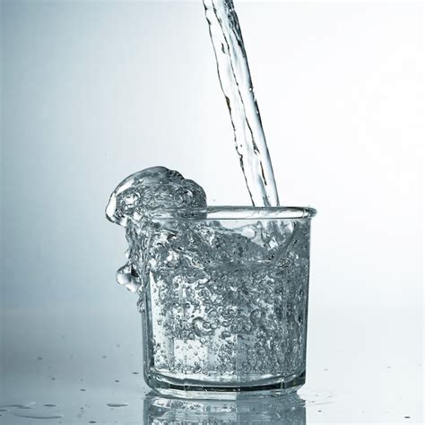 El agua pura fresca y fría se vierte en un vaso. agua purificada en un vaso sobre una mesa gris ...