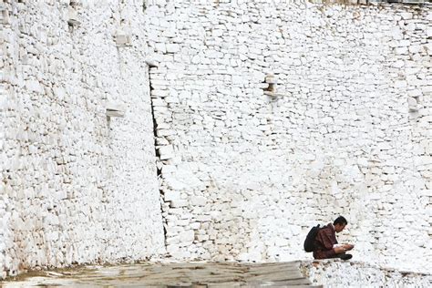 Bhutanese man checking his mobile phone next a white stone wall.