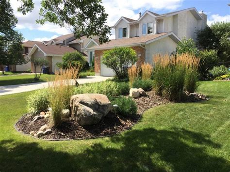 Updated Front yard berm with round boulders wood mulch and plants | The Lawn Salon