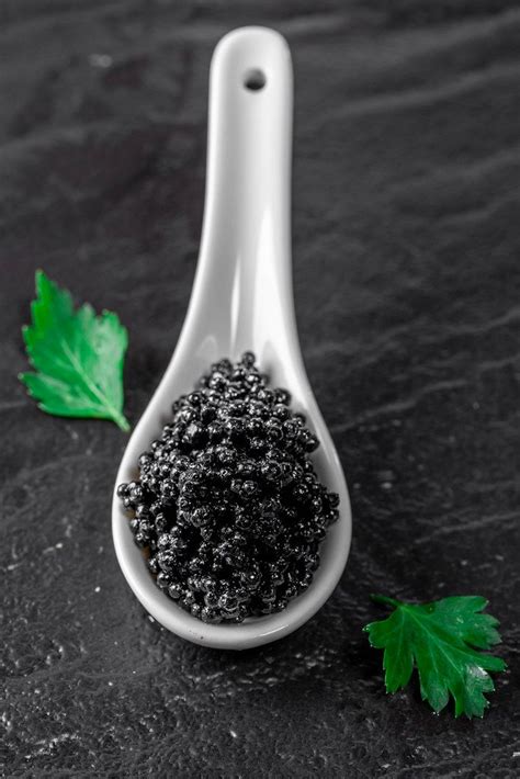Black and red caviar with butter and spoon on black stone background. Top view - Creative ...