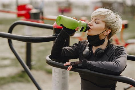 Sportswoman with mask on chin drinking water during street workout · Free Stock Photo