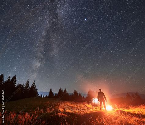 Silhouette of male tourist standing near campfire under beautiful night ...