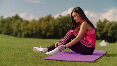 Asian woman tying laces on her sneakers. Cute girl stretching on yoga mat and tying shoelaces in ...