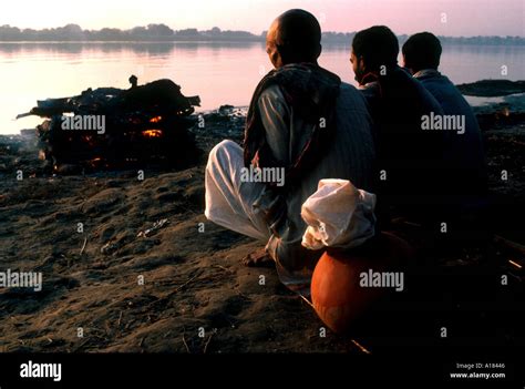 Three figures perform cremation on bank of the River Ganges India J H C ...