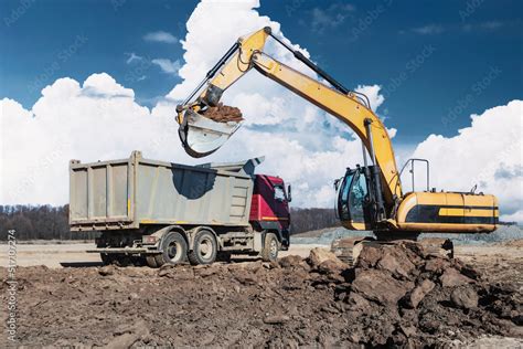 Foto de A powerful crawler excavator loads the earth into a dump truck against the blue sky ...