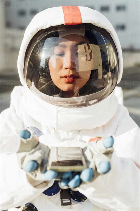 Female astronaut in space suit looking at smart phone in hands during sunny day stock photo