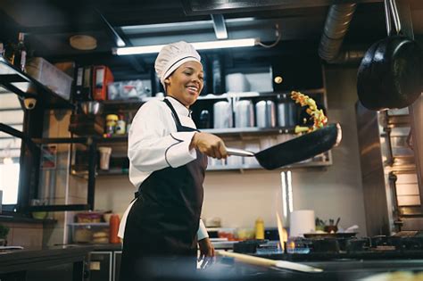 Happy Black Female Chef Preparing Food In Frying Pan At Restaurant ...